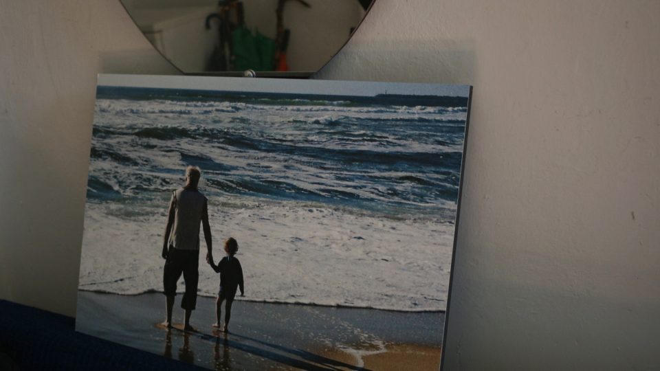 Fotografie od Moniky Štreitové Jindřicha Štreita s vnukem u oceánu v Portugalsku umístěná pod zrcadlem v předsíni na Sovinci